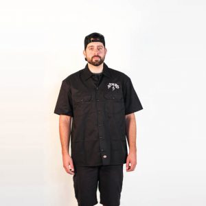Male modeling black Dickies short sleeved collared shirt with Heady Topper logo on the back. Front view. The Alchemist logo in white over front left pocket. Front view.