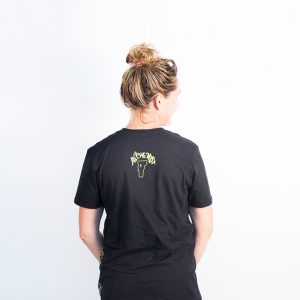 Female modeling black tee with hop wreath on wearer's left side. Back view shows Alchemist logo and state of Vermont.